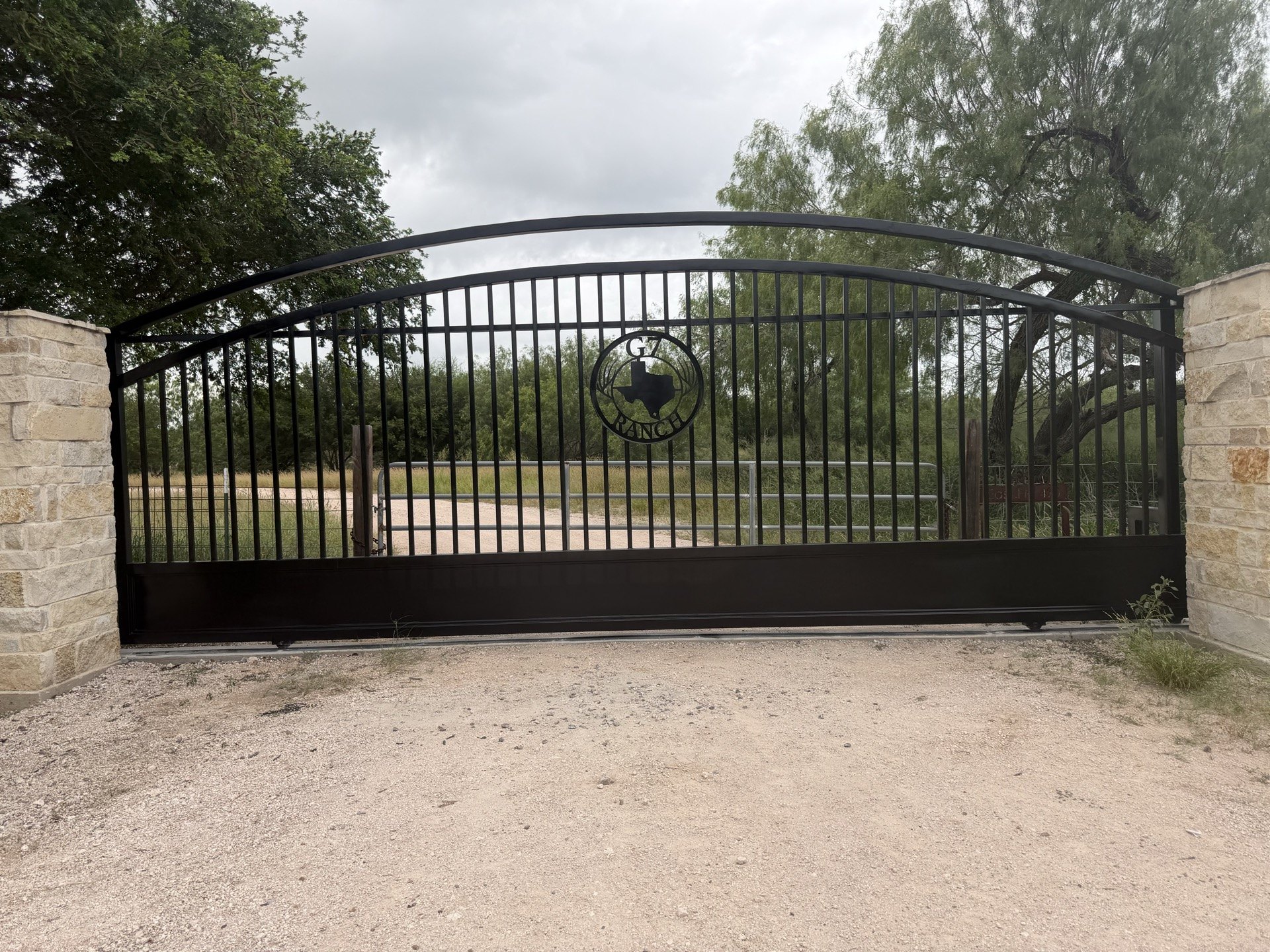 Black arched driveway gate between stone columns in Edinburg