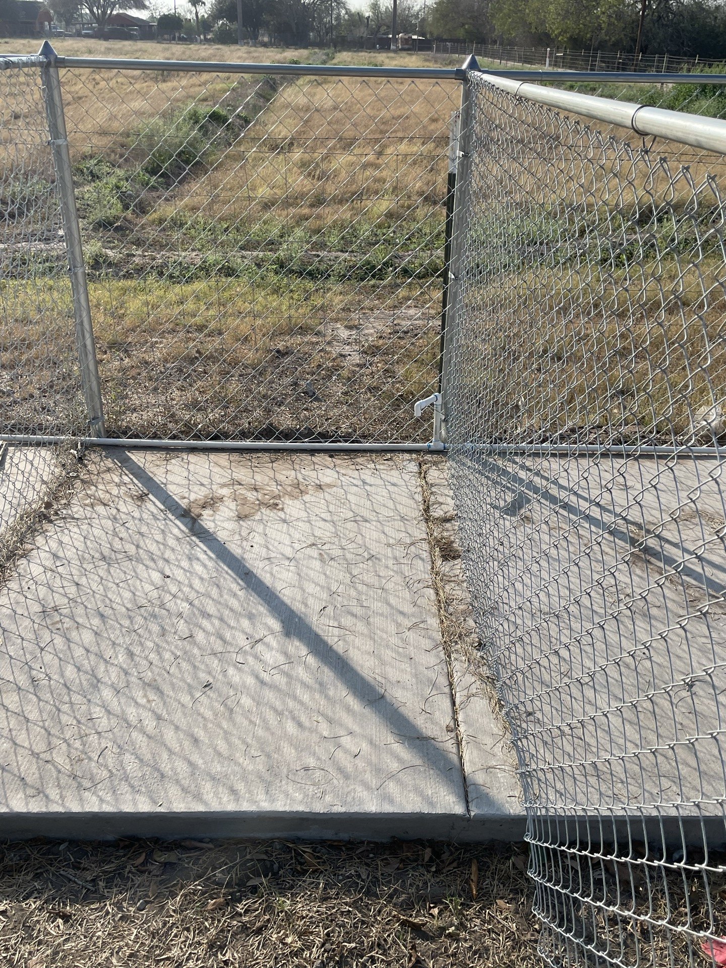 Open chain-link enclosure gate beside a concrete floor