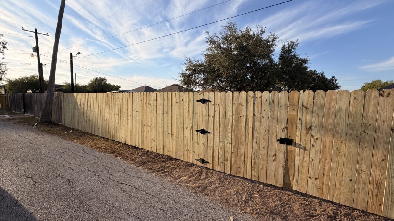 Wood privacy fence and matching gates with black hinges along a La Feria property.