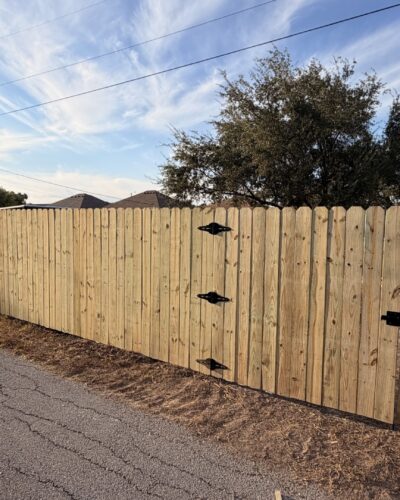 Wood privacy fence and matching gates with black hinges along a La Feria property.