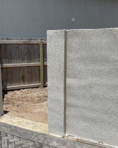 Stucco wall sections framing a yard entrance beside a paved driveway.